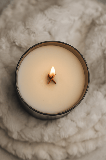 Candle in a glass container with a wooden wick, lit on a textured surface.