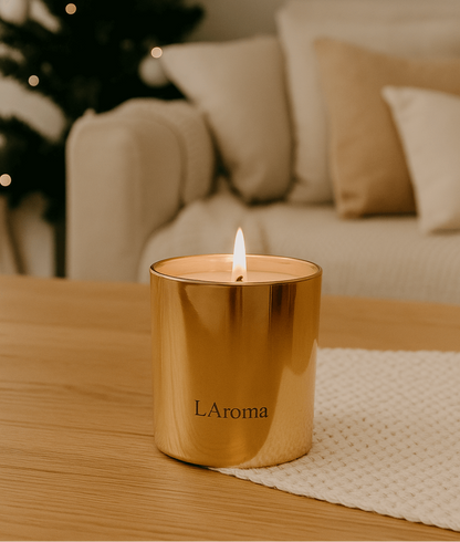 Gold candle labeled 'LáRoma' on a wooden table with a blurred Christmas tree and sofa in the background.